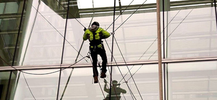 Employee hanging by ropes while reflected in high rise windows